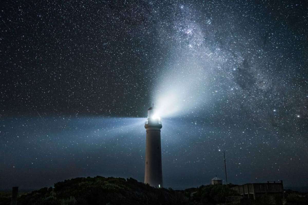 A picture of a lighthouse with the backdrop of a dark night and a multitude of stars